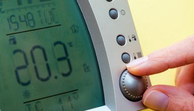 Dyma lun agos o fysedd yn addasu thermostat domestig i dymheredd uchel.