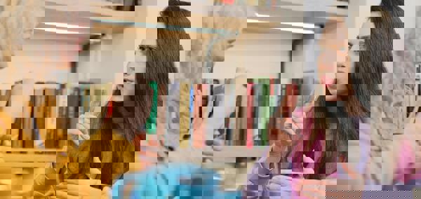 Dwy fenyw yn eistedd wrth fwrdd gyda phot o de, yn cael sgwrs drwy ddefnyddio Iaith Arwyddion Prydain.