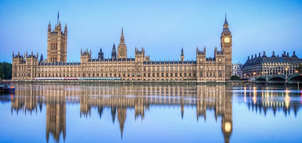 Dau Dŷ Senedd y Deyrnas Unedig yn ystod y dydd o’r ochr draw i Afon Tafwys, a’u hadlewyrchiad yn y dŵr. 