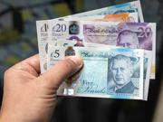 Llaw yn dal amrywiaeth o nodiadau banc y DU, gan gynnwys £5, £10 a £20.