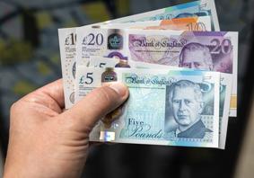 Llaw yn dal amrywiaeth o nodiadau banc y DU, gan gynnwys £5, £10 a £20.