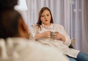 Menyw yn dal diod yn eistedd gyferbyn â pherson arall 