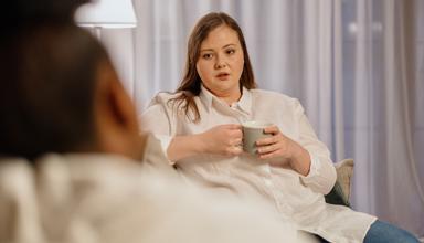 Menyw yn dal diod yn eistedd gyferbyn â pherson arall 