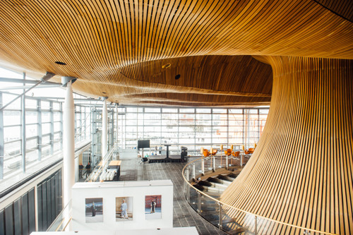 Mae’r ddelwedd yn dangos twndis pren y Senedd a thri phaentiad ar banel arddangos gwyn yn ardal yr Oriel.