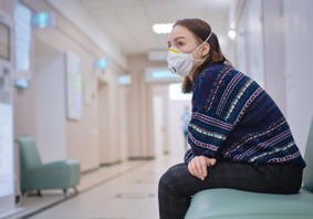 Woman sitting alone in a hospital corridor with a face mask on