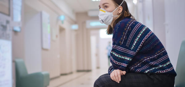 Woman sitting alone in a hospital corridor with a face mask on