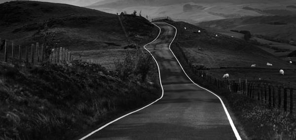 Llun yn dangos creigiau mawr danheddog ar lan y môr. Yn y pellter, gellir gweld amlinelliad bras o’r môr. Mae'r awyr lwyd, dywyll yn llawn cymylau.