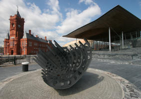 Llun o adeiladau'r Senedd a'r Pierhead, gyda cherflun yn y blaen. 
