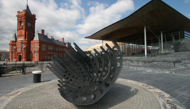 Llun o adeiladau'r Senedd a'r Pierhead, gyda cherflun yn y blaen. 
