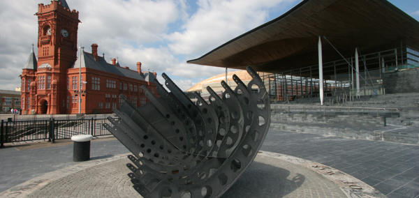 Llun o adeiladau'r Senedd a'r Pierhead, gyda cherflun yn y blaen. 