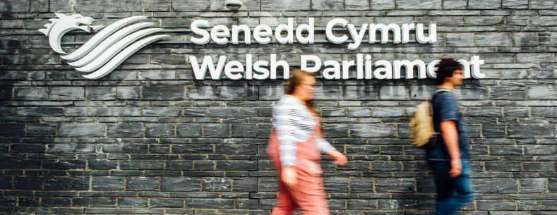 People walking past the Senedd signage