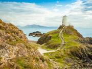 Ynys Llanddwyn, goleudy, gyda'r môr a'r mynyddoedd yn y cefndir.