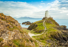 Ynys Llanddwyn, goleudy, gyda'r môr a'r mynyddoedd yn y cefndir.