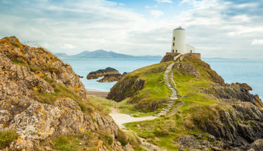 Ynys Llanddwyn, goleudy, gyda'r môr a'r mynyddoedd yn y cefndir.