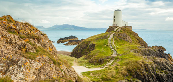 Ynys Llanddwyn, goleudy, gyda'r môr a'r mynyddoedd yn y cefndir.