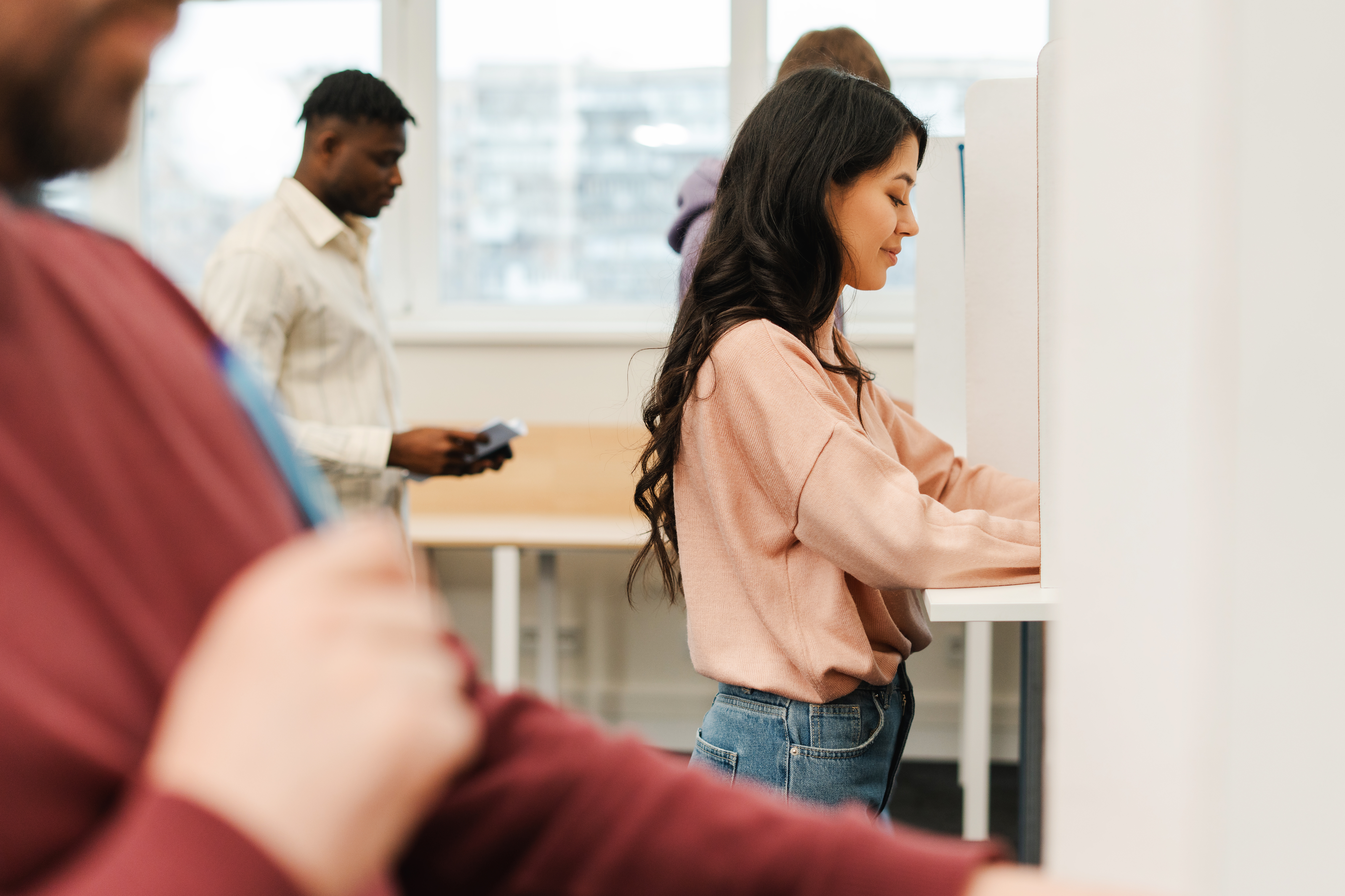 Llun o fenyw ifanc yn sefyll mewn bwth pleidleisio yn bwrw ei phleidlais.